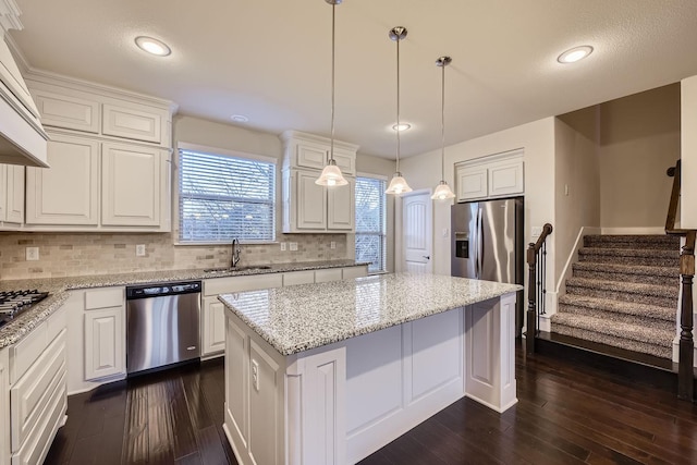 kitchen featuring a kitchen island, sink, white cabinets, hanging light fixtures, and stainless steel appliances