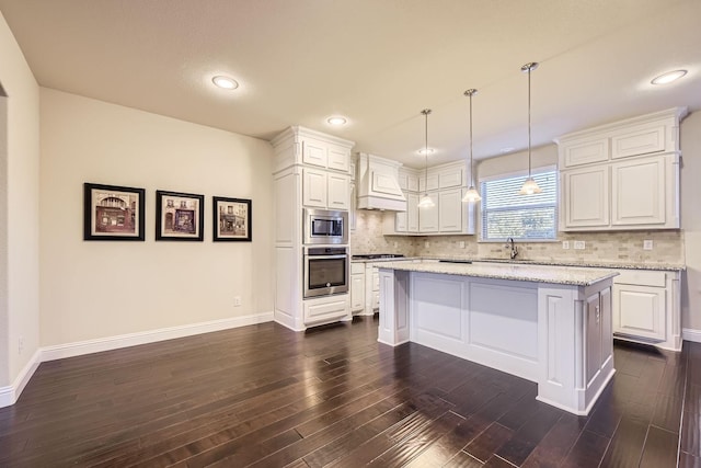 kitchen with decorative backsplash, light stone counters, stainless steel appliances, a center island, and white cabinetry