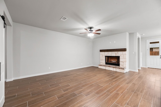 unfurnished living room featuring a barn door, a fireplace, a ceiling fan, visible vents, and wood finished floors