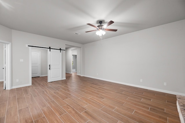 unfurnished bedroom with visible vents, a barn door, light wood-style flooring, and baseboards