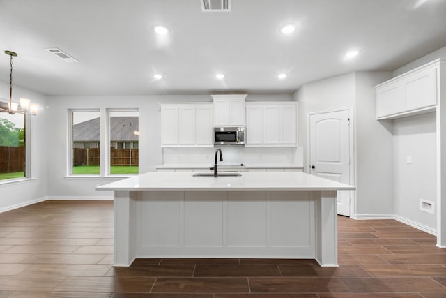 kitchen featuring stainless steel microwave, a sink, wood tiled floor, light countertops, and an island with sink