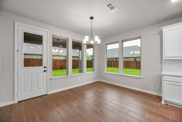 unfurnished dining area with an inviting chandelier, wood finished floors, visible vents, and baseboards