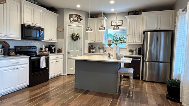 kitchen featuring dark wood-type flooring, hanging light fixtures, a center island, black appliances, and white cabinets