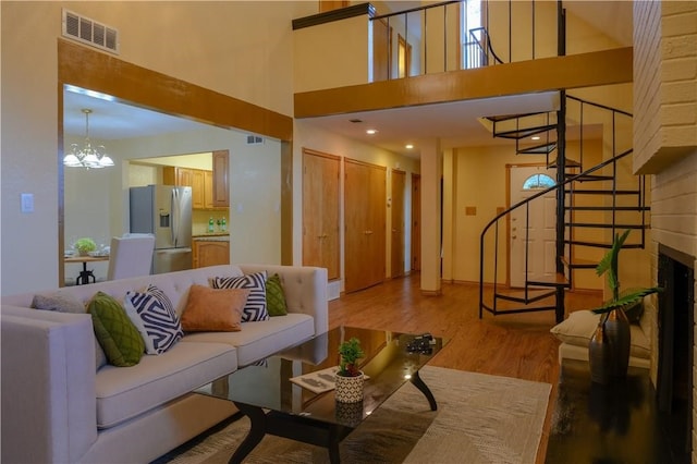 living room with hardwood / wood-style flooring, a notable chandelier, a high ceiling, and a brick fireplace