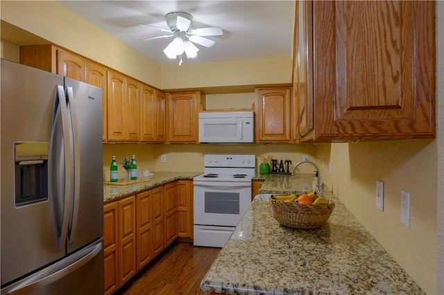 kitchen featuring white appliances, sink, ceiling fan, light stone counters, and wood-type flooring