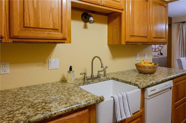 kitchen featuring white dishwasher, light stone counters, and sink