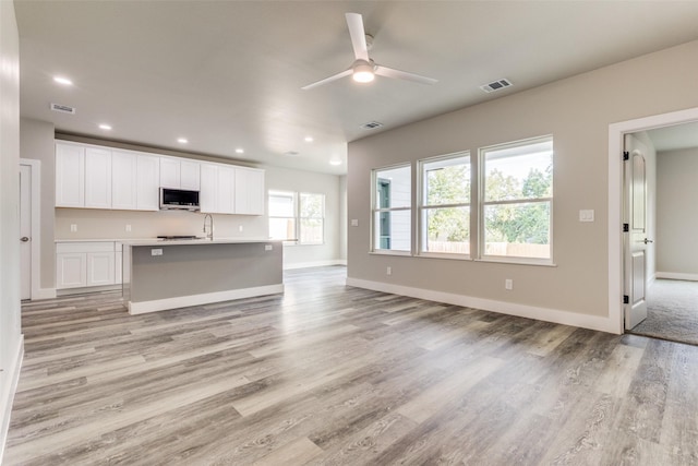 kitchen featuring white cabinetry, ceiling fan, a kitchen island with sink, and light wood-type flooring