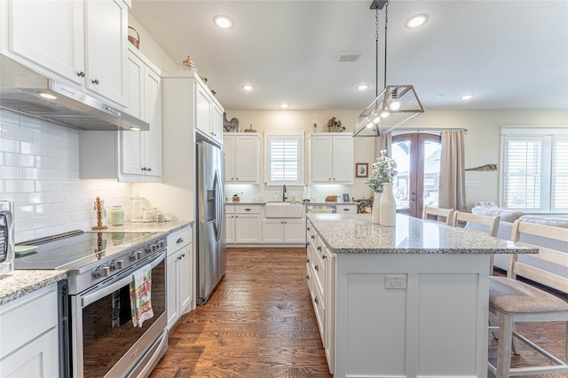 kitchen featuring a kitchen bar, appliances with stainless steel finishes, white cabinetry, and light stone countertops