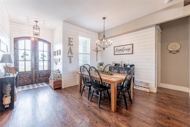 dining space with a chandelier, wood walls, dark wood-type flooring, and french doors