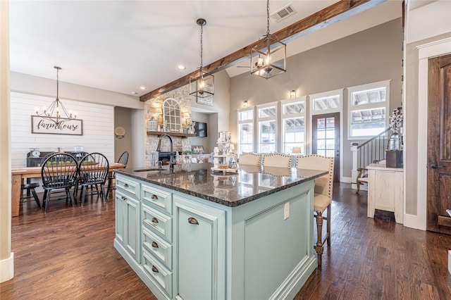 kitchen with a kitchen island with sink, sink, green cabinetry, decorative light fixtures, and beam ceiling