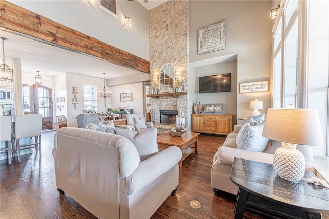 living room with a chandelier, a towering ceiling, a fireplace, and dark wood-type flooring