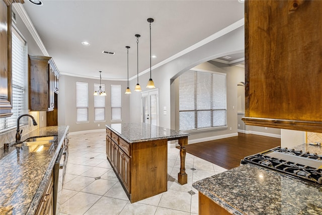 kitchen featuring dark stone counters, sink, light tile patterned floors, ornamental molding, and a kitchen island