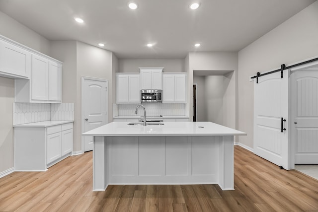 kitchen featuring a barn door, light wood-type flooring, stainless steel microwave, and a sink