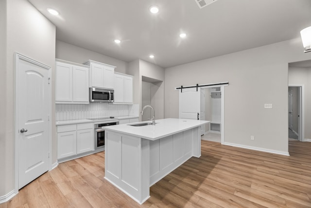 kitchen with white cabinetry, a sink, appliances with stainless steel finishes, a barn door, and backsplash