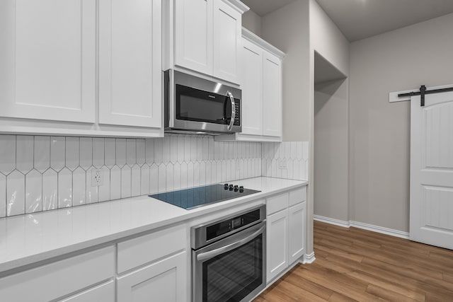 kitchen with a barn door, light wood-type flooring, light countertops, white cabinets, and appliances with stainless steel finishes