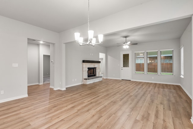 unfurnished living room with ceiling fan with notable chandelier, a stone fireplace, baseboards, and light wood-style floors
