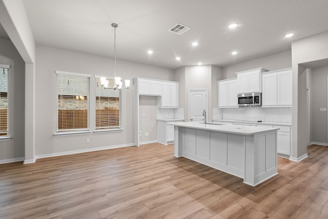 kitchen featuring stainless steel microwave, a sink, light wood-style floors, a chandelier, and backsplash