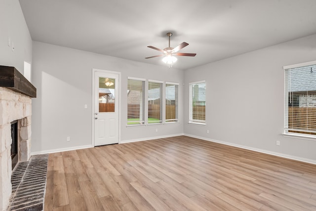 unfurnished living room with a fireplace, a ceiling fan, light wood-style flooring, and baseboards