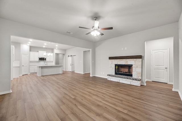 unfurnished living room with visible vents, ceiling fan with notable chandelier, light wood-style floors, and a fireplace