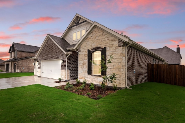 view of front of house with concrete driveway, stone siding, a lawn, an attached garage, and fence