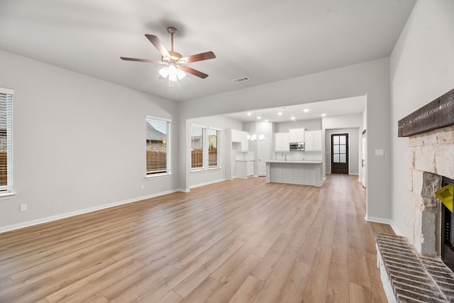 unfurnished living room with ceiling fan, a wealth of natural light, light wood finished floors, and a fireplace with raised hearth