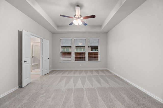 unfurnished bedroom featuring connected bathroom, a raised ceiling, a ceiling fan, light carpet, and baseboards