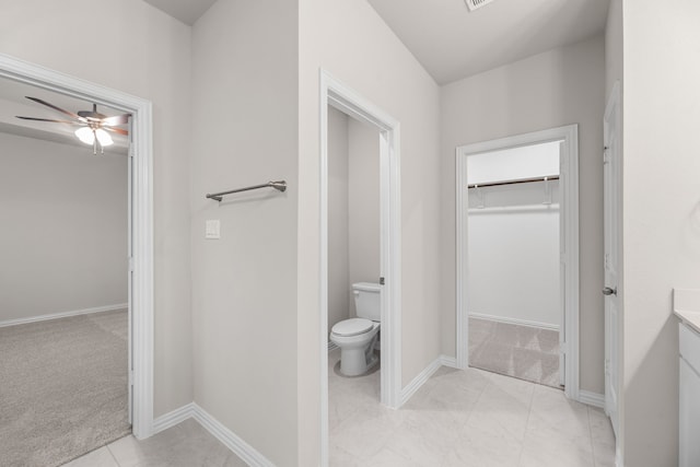 bathroom featuring vanity, toilet, a ceiling fan, baseboards, and a spacious closet