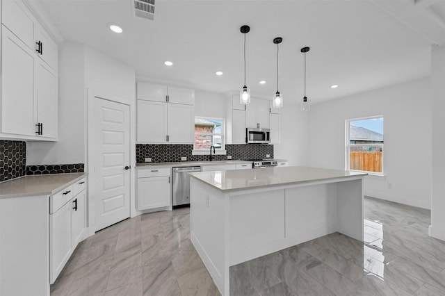 kitchen with appliances with stainless steel finishes, a center island, decorative light fixtures, white cabinetry, and sink