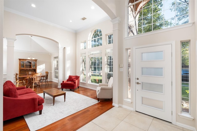 foyer with crown molding, a towering ceiling, light hardwood / wood-style floors, and decorative columns