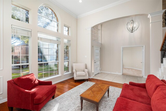 living room featuring ornamental molding, light hardwood / wood-style floors, a notable chandelier, and a high ceiling