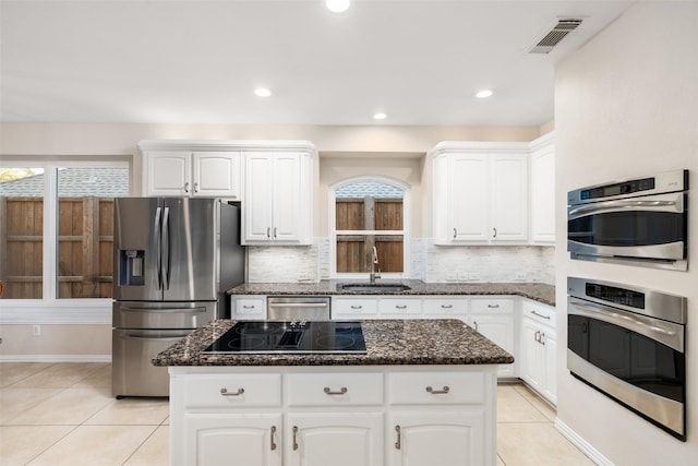 kitchen featuring a center island, dark stone counters, sink, appliances with stainless steel finishes, and white cabinetry