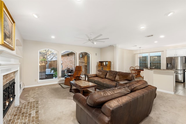 living room with a tiled fireplace, ceiling fan, and light carpet