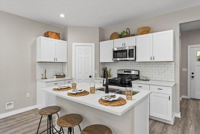 kitchen with a kitchen breakfast bar, an island with sink, appliances with stainless steel finishes, tasteful backsplash, and white cabinetry