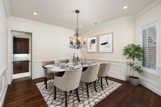 dining area with dark wood-type flooring, ornamental molding, and an inviting chandelier