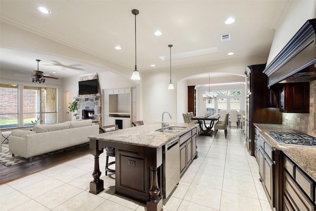 kitchen featuring appliances with stainless steel finishes, decorative light fixtures, an island with sink, sink, and light stone counters