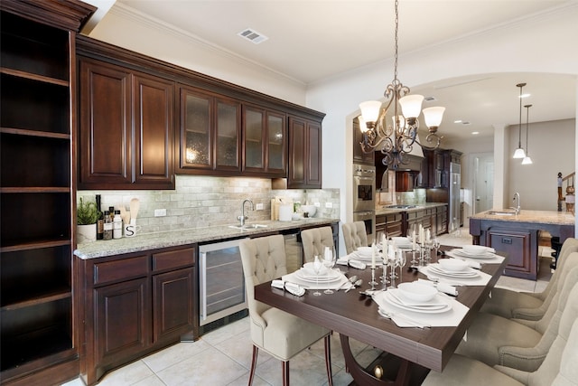 kitchen featuring pendant lighting, sink, light stone counters, wine cooler, and dark brown cabinetry