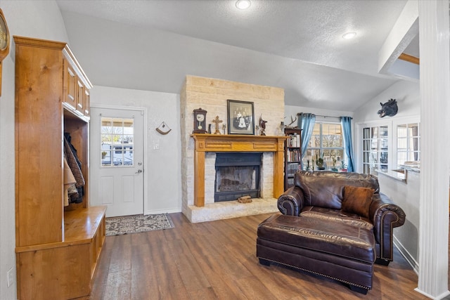 living room with dark hardwood / wood-style flooring, vaulted ceiling, a brick fireplace, and a textured ceiling