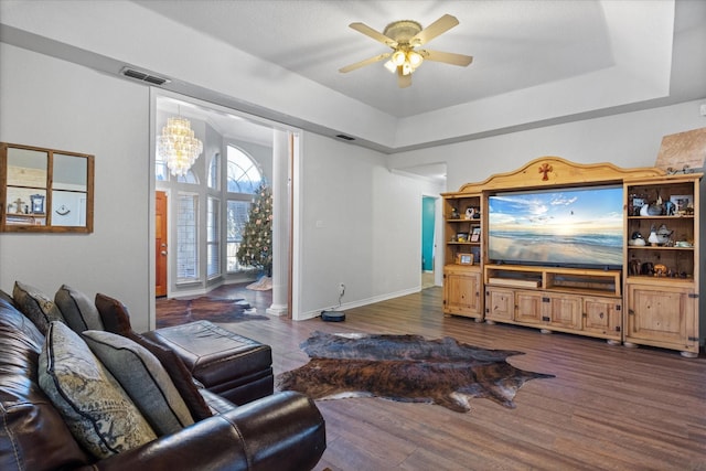 living room with a raised ceiling, ceiling fan with notable chandelier, and dark hardwood / wood-style flooring