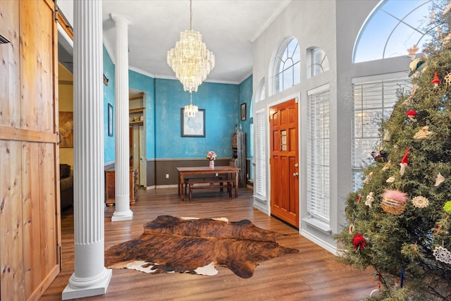 foyer entrance featuring crown molding, wood-type flooring, decorative columns, and a notable chandelier