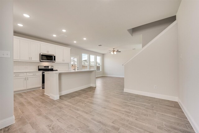 kitchen with backsplash, white cabinets, ceiling fan, an island with sink, and stainless steel appliances