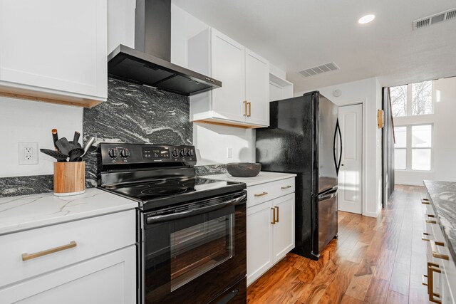 kitchen featuring visible vents, black appliances, light wood-style floors, and wall chimney range hood