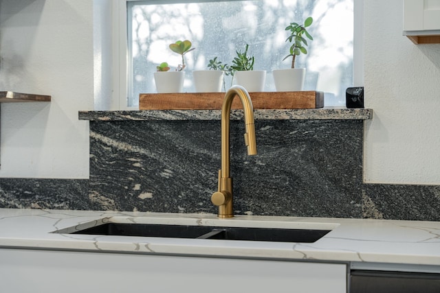 kitchen with a sink, dishwashing machine, light stone counters, and white cabinetry