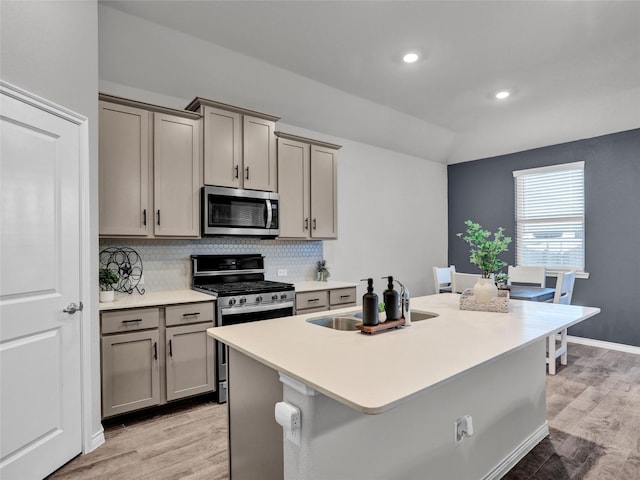 kitchen featuring backsplash, an island with sink, light hardwood / wood-style floors, gray cabinets, and appliances with stainless steel finishes