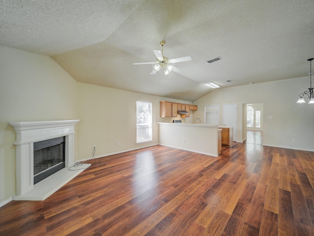 unfurnished living room featuring ceiling fan with notable chandelier, lofted ceiling, and dark wood-type flooring