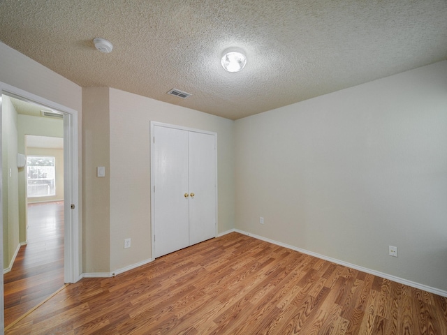 unfurnished bedroom with a textured ceiling, hardwood / wood-style flooring, and a closet