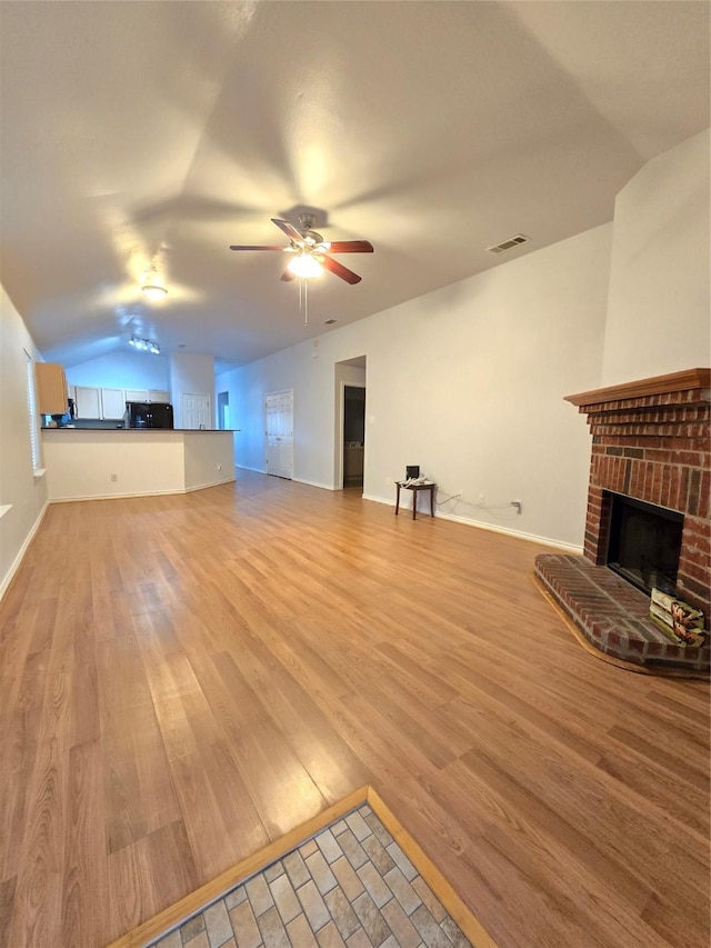 unfurnished living room with ceiling fan, a fireplace, vaulted ceiling, and light wood-type flooring