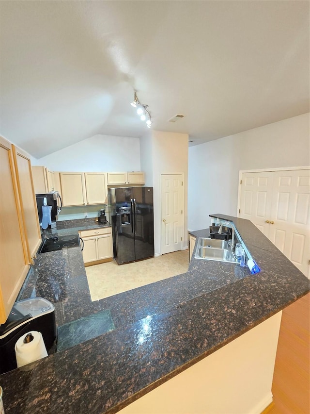 kitchen with light brown cabinetry, black fridge, sink, dark stone countertops, and lofted ceiling