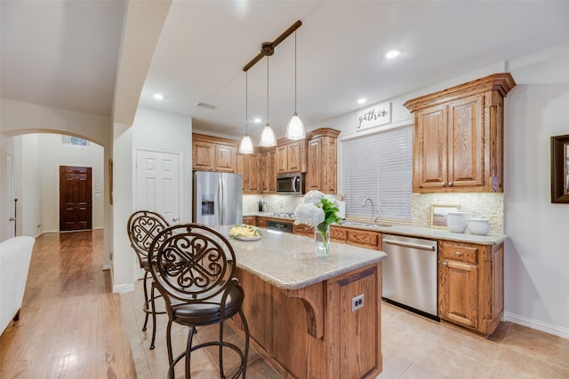 kitchen with tasteful backsplash, stainless steel appliances, sink, pendant lighting, and a kitchen island