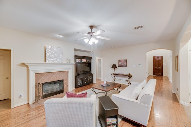 living room featuring a tiled fireplace, ceiling fan, and light wood-type flooring