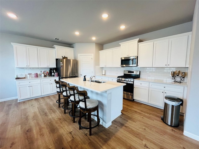 kitchen featuring a breakfast bar area, stainless steel appliances, a sink, light wood finished floors, and an island with sink